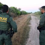 Two U.S. Border Patrol officers observing a dirt path.