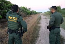 Two U.S. Border Patrol officers observing a dirt path.