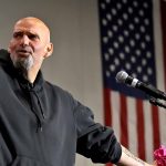 Bald man in black hoodie speaks at microphone.