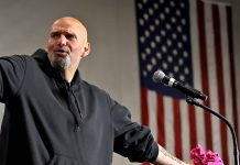 Bald man in black hoodie speaks at microphone.