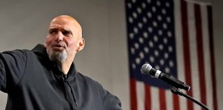 Bald man in black hoodie speaks at microphone.