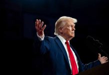 Person in suit gestures while speaking at podium.