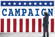 Man pointing at "CAMPAIGN" sign with stars and stripes.