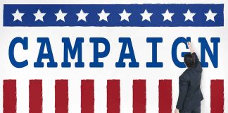 Man pointing at "CAMPAIGN" sign with stars and stripes.