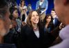 Smiling woman surrounded by people and camera crew.