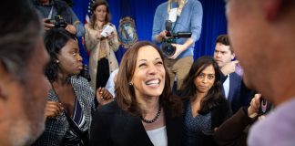 Smiling woman surrounded by people and camera crew.