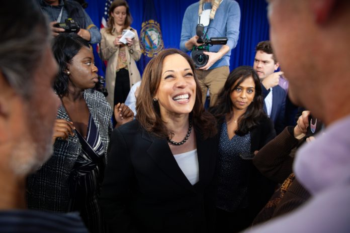 Smiling woman surrounded by people and camera crew.