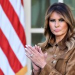 Woman standing near American flag, clapping her hands.