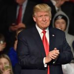 Man in suit clapping at public event.