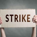 Two hands holding a cardboard sign saying "STRIKE".