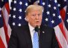 Man speaking at podium with American flags behind.