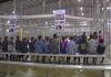 People sitting on benches inside a fenced facility.