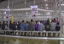 People sitting on benches inside a fenced facility.