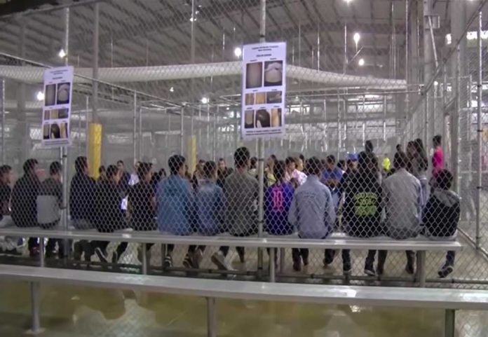 People sitting on benches inside a fenced facility.