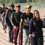 Line of people walking on a dirt road.