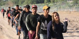 Line of people walking on a dirt road.