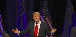 Man speaking at podium with flags behind him.