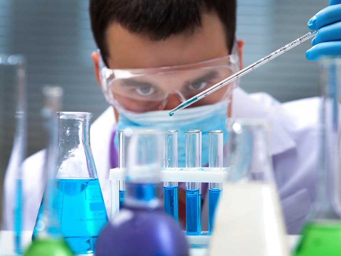 Scientist pipetting blue liquid into test tubes.