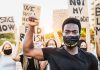 Protester raises fist, wears mask, signs in background.