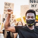 Protester raises fist, wears mask, signs in background.