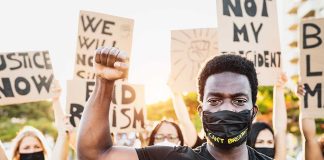 Protester raises fist, wears mask, signs in background.