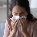 Woman sneezing into a tissue indoors.