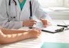 Doctor discussing with patient, holding clipboard on desk.