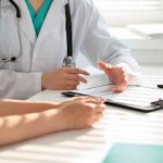 Doctor discussing with patient, holding clipboard on desk.