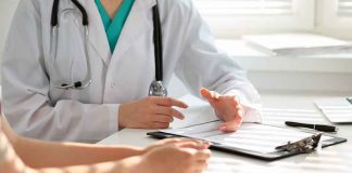 Doctor discussing with patient, holding clipboard on desk.