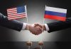Two people shaking hands beneath US and Russian flags