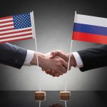 Two people shaking hands beneath US and Russian flags