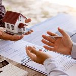 Two people discussing real estate contract with model house