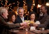 People laughing while clinking glasses at a bar