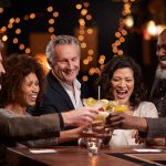 People laughing while clinking glasses at a bar
