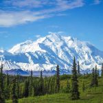 Snowcovered mountain under blue sky with green foreground