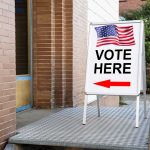 Voting sign outside building with American flag visible