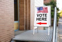 Voting sign outside building with American flag visible
