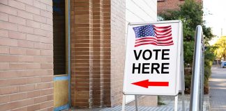Voting sign outside building with American flag visible