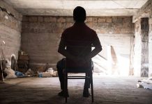 Person tied to chair in dimly lit room