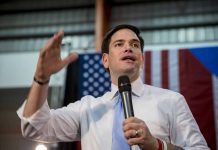 Man speaking with microphone indoors near flags
