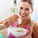 Woman smiling eating salad with fork indoors