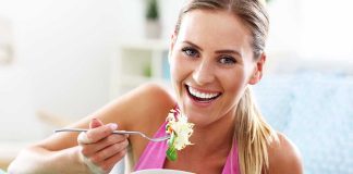Woman smiling eating salad with fork indoors