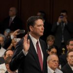 A man in suit raising hand, surrounded by crowd.