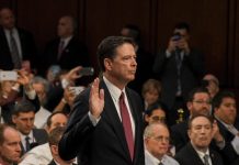 A man in suit raising hand, surrounded by crowd.