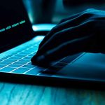 Hand typing on laptop with code on screen