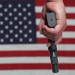 Hand holding gun against American flag backdrop