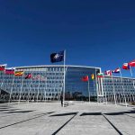 Flags outside NATO headquarters building under clear blue sky