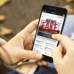 Person holding smartphone displaying fake news notification
