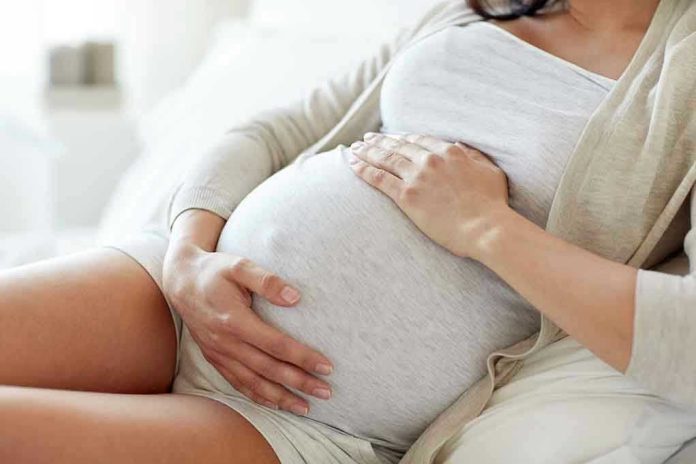 564114571 Pregnant woman holding her belly, sitting comfortably.