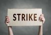 Two hands holding a cardboard sign saying STRIKE
